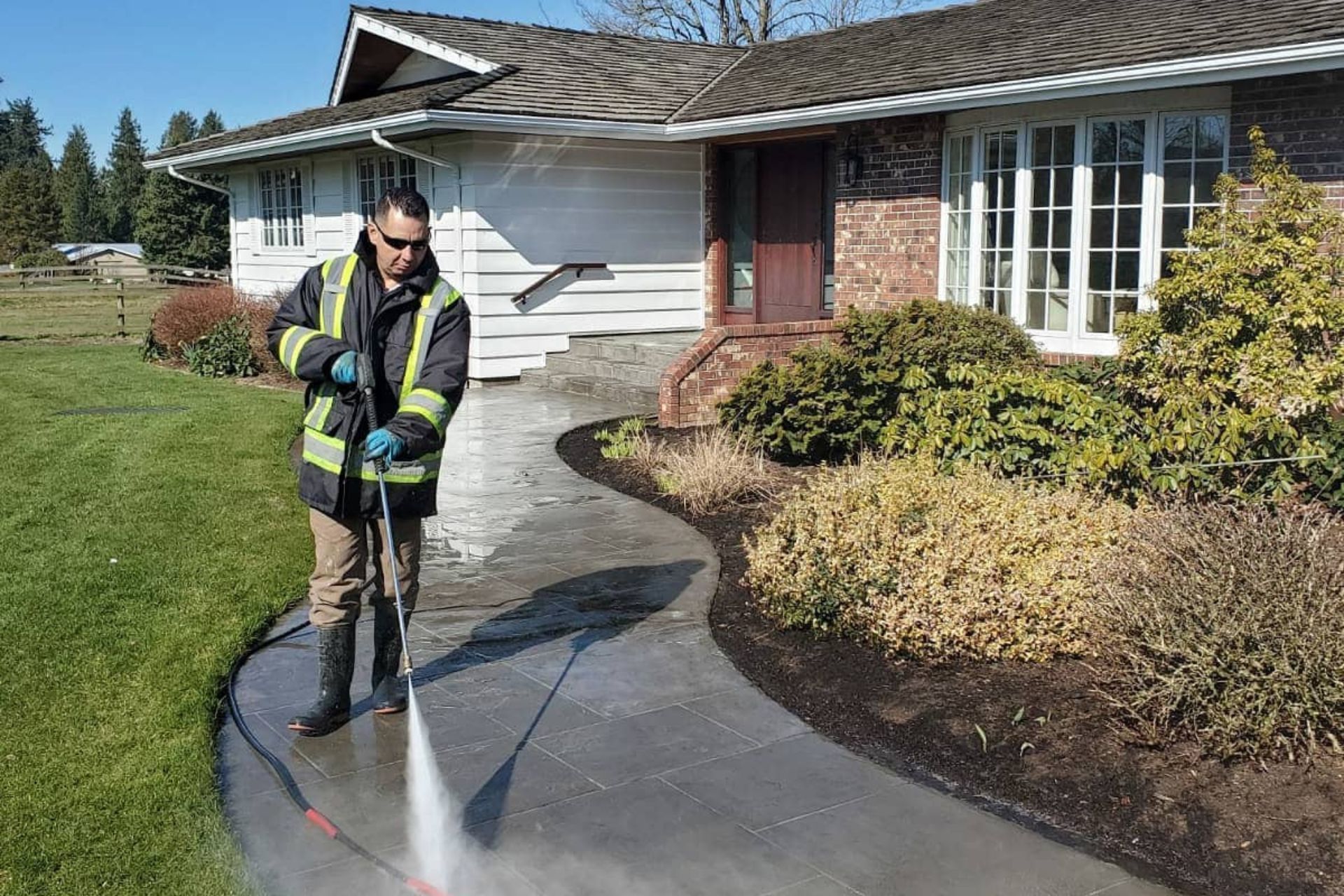 Technician pressure washing a stamped concrete driveway in high-visibility gear